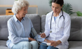 istockphoto-1267012037-612x612 Pleasant young nurse in medical uniform measuring blood pressure of elderly senior retired patient at checkup meeting at home. Skilled caregiver visiting middle aged woman, geriatric help concept.