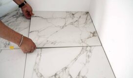 Construction worker placing large format white porcelain tiles with marble effect on the floor during renovation work