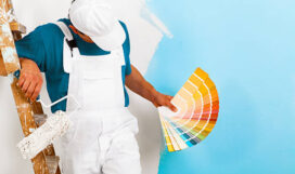 portrait of painter man with paintroller and wooden vintage ladder showing a color palette, on half painted wall